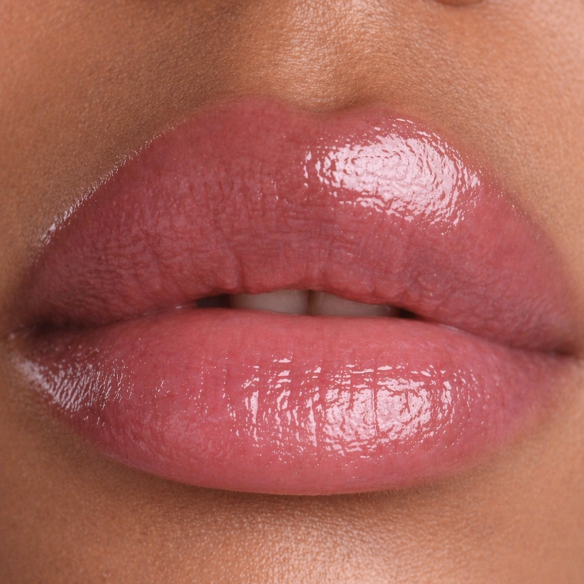 Close-up of glossy pink lips wearing a lip product, showing the texture and color on the lips against warm skin tones.